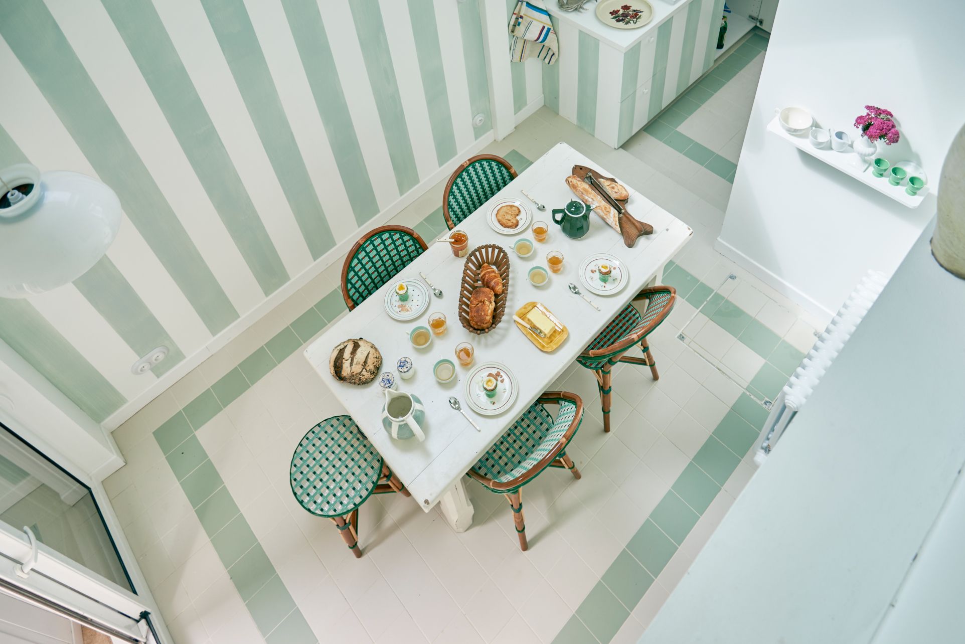 Salle à manger, couleur vert céladon, une table dressée avec du pain, du jus, des croissant, et du thé.